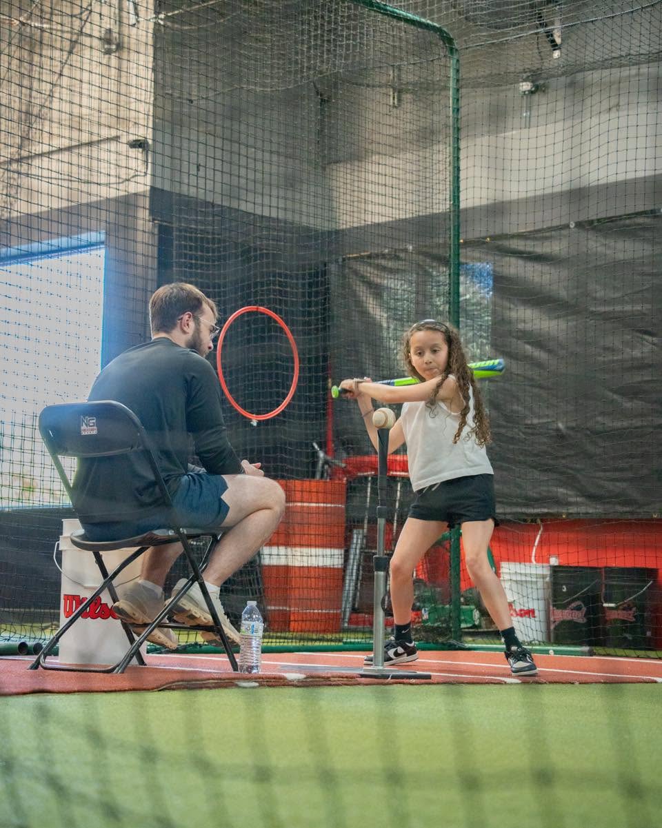 Young athlete practicing her swing off a tee with a NexGen Sports coach in the batting cage